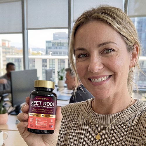 Woman holding LIFEPLEMENT Beetroot Supplements in office setting.